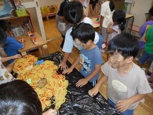 5歳児が3歳児に毛糸で作った焼きそばを渡す