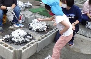アルミホイルで包んだサツマイモをかまどに入れている子どもの写真