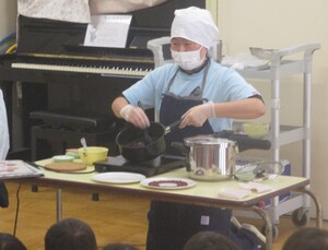 　食育集会で豆の仲間（豆エイト）の話、小豆煮の様子を見る子どもの姿